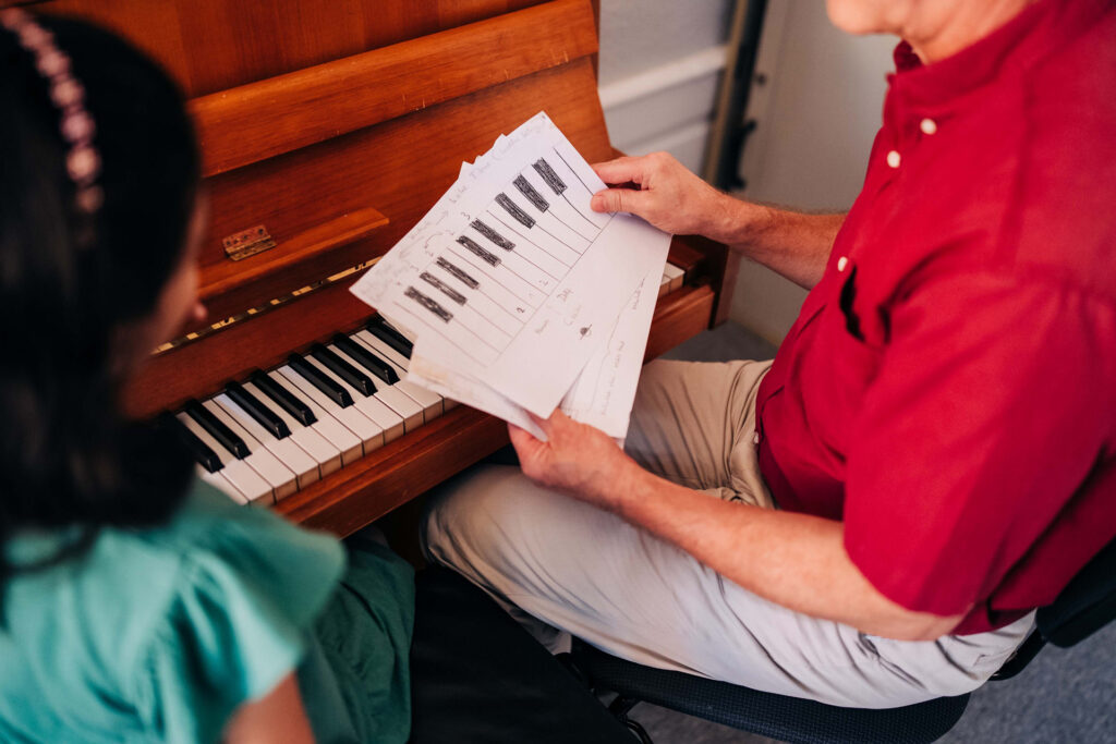 Foto von Klaviernoten, die sich der Lehrer gemeinsam mit der Schülerin ansieht