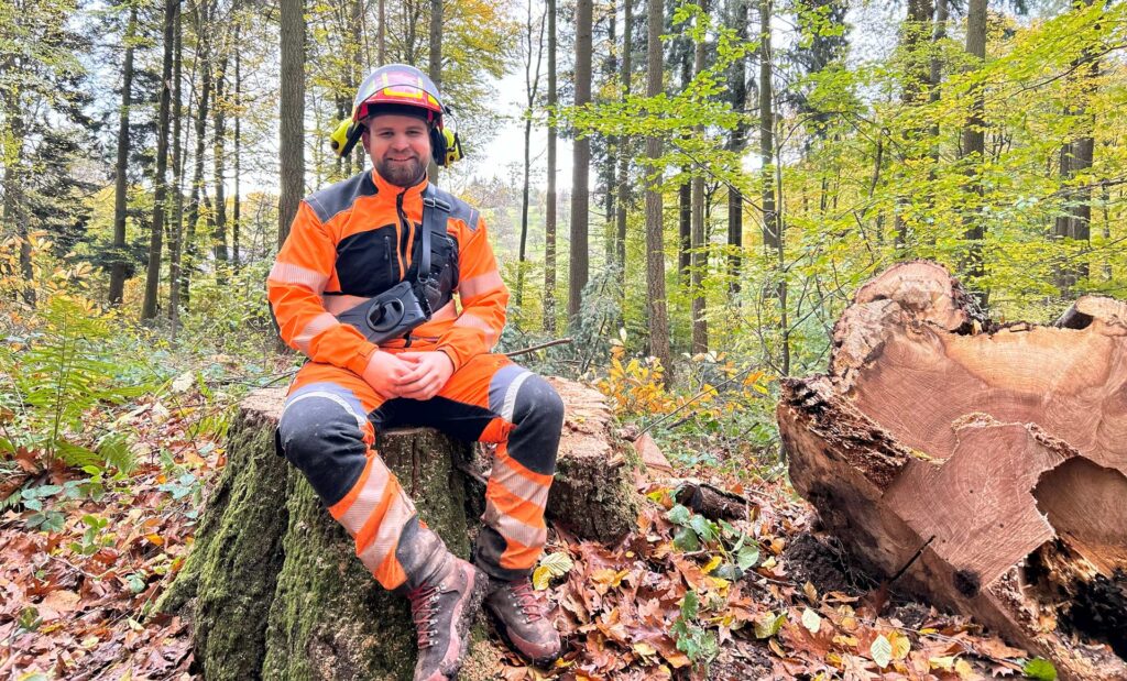 Marvin Kronauer sitzt auf einem Stamm im Wald