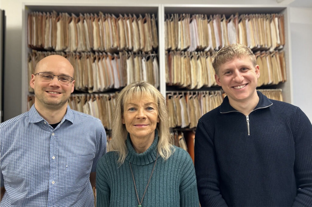 Das Projektteam der E-Akten Implementierung lächelt in die Kamera und steht vor einem Aktenschrank.