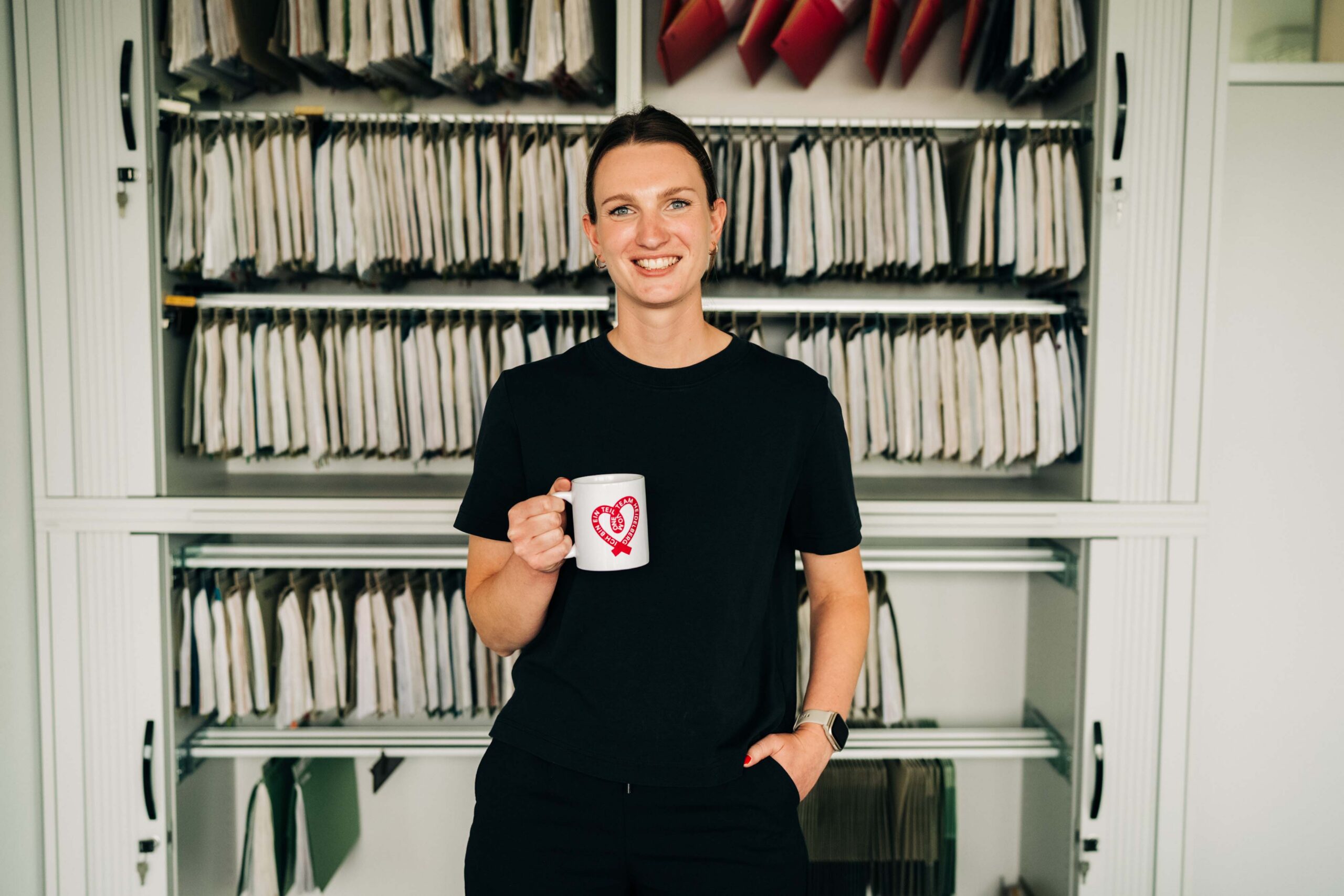 Mitarbeiterin vor Aktenschrank mit Tasse in der Hand
