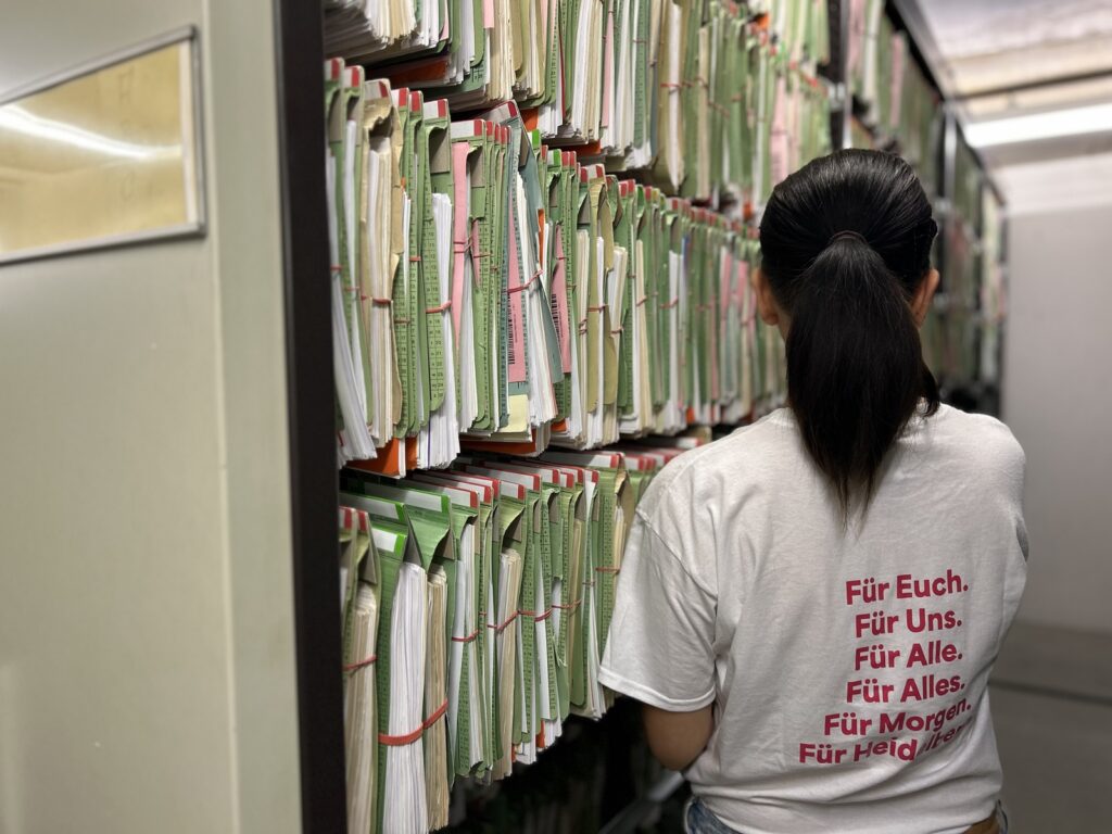 Eine Mitarbeiterin steht vor einem Aktenschrank mit Blick zu den Akten