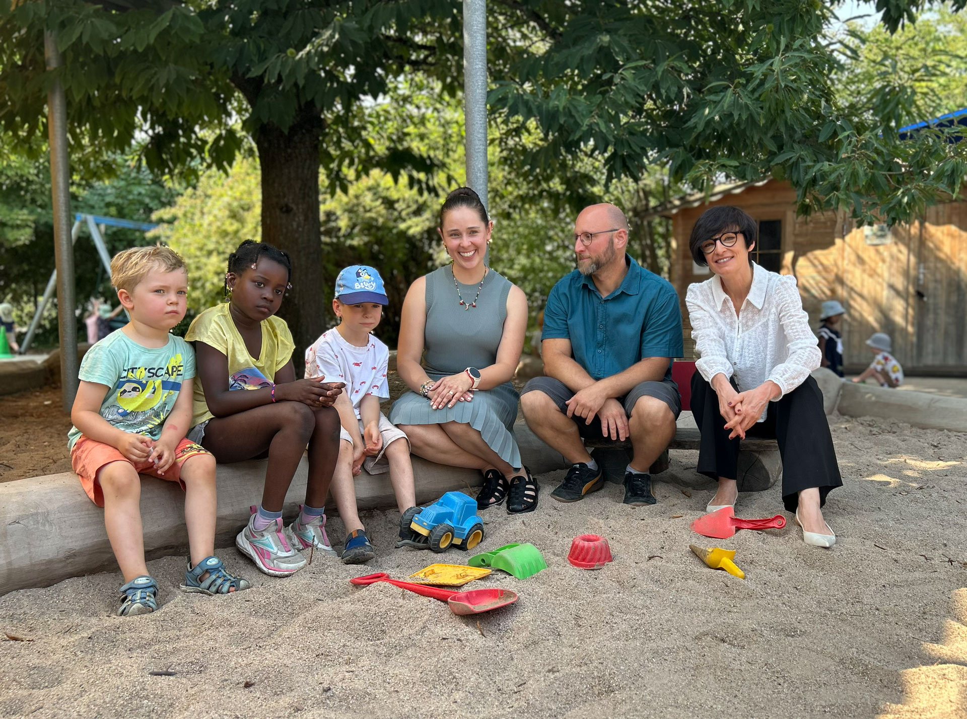 Kolumbianische Erzieherin mit Frau Jansen und Sven Weiß im Sandkasten mit Kindern